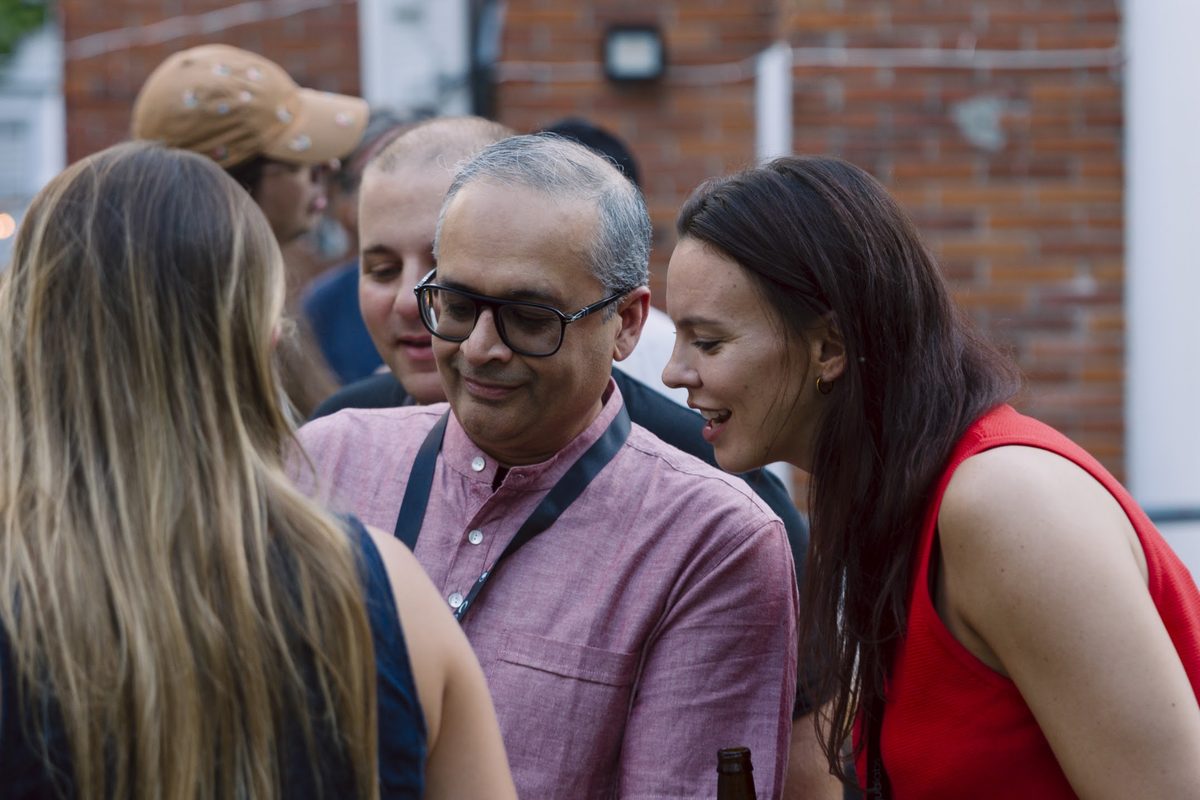 Three campers leaning in over a phone, laughing, at a 2026 evening gathering