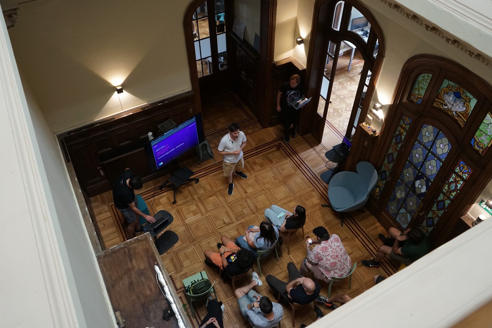 The final demo of Summer Projects 2026, seen from the floor above: someone presenting beside a screen that reads Summer Projects 2026 Final Demo, with the room watching