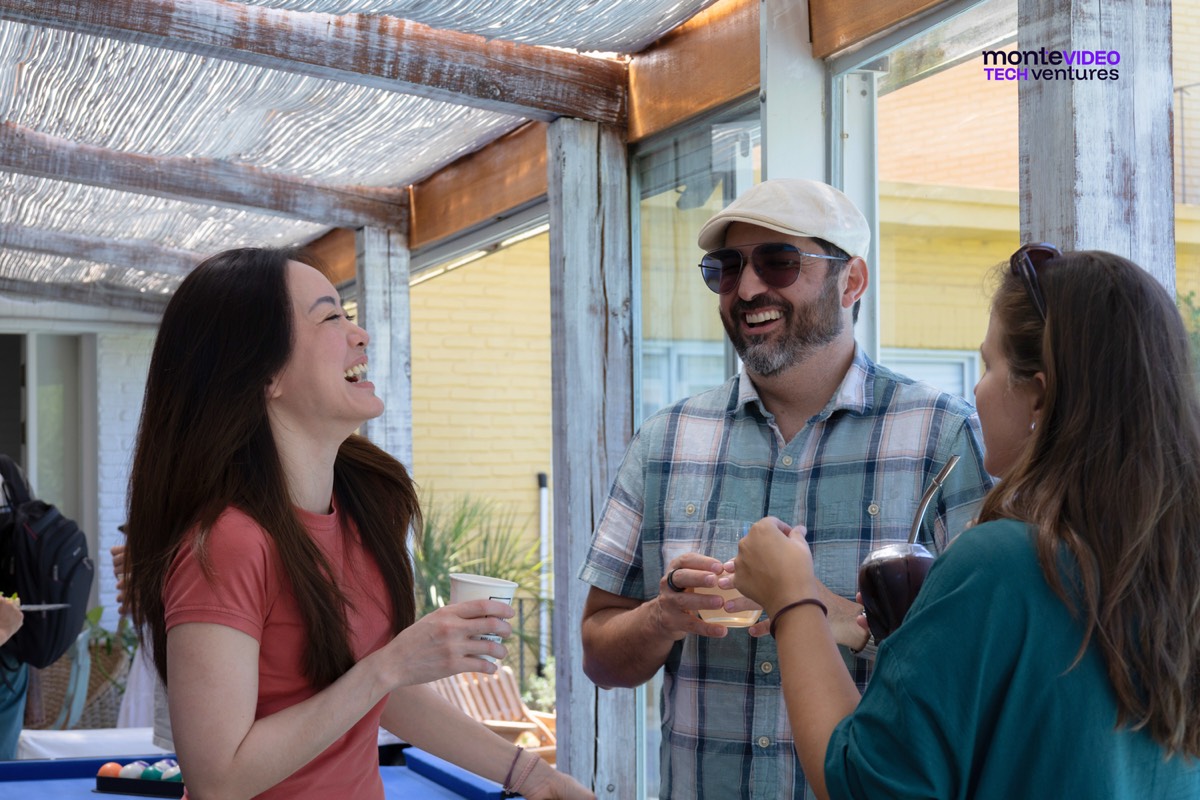 Three people from the 2026 Innovation Track laughing over mate and coffee under a pergola