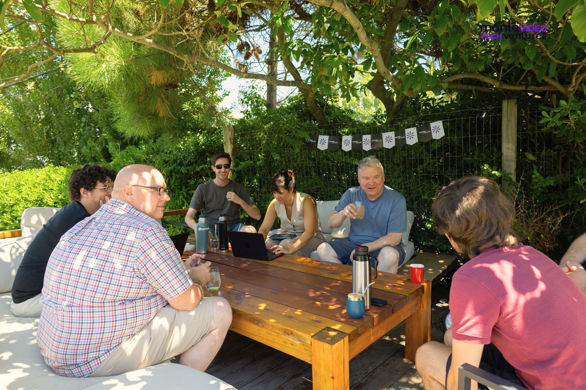 A group from the 2026 Innovation Track sitting outdoors around a low table, with laptops, mate and a thermos