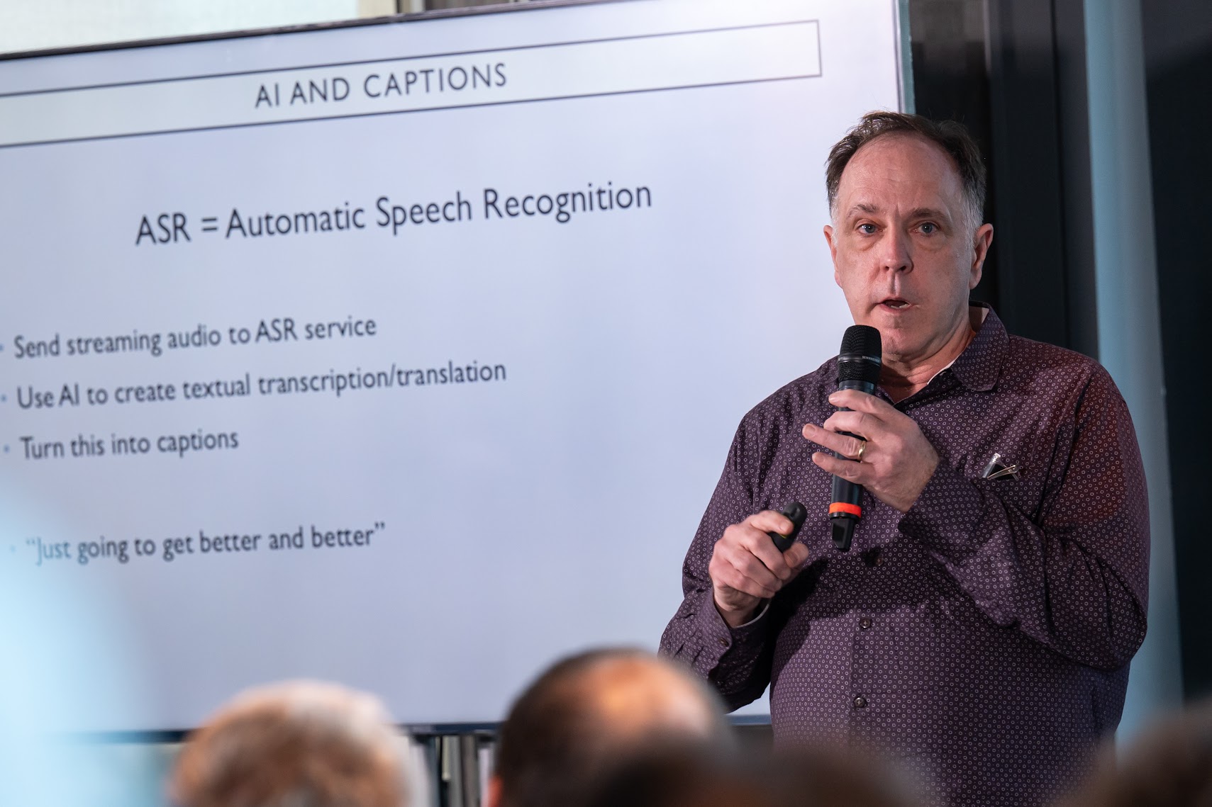 Speaker presenting a slide titled “AI and captions — ASR = Automatic Speech Recognition” at MonteVIDEO Tech Day