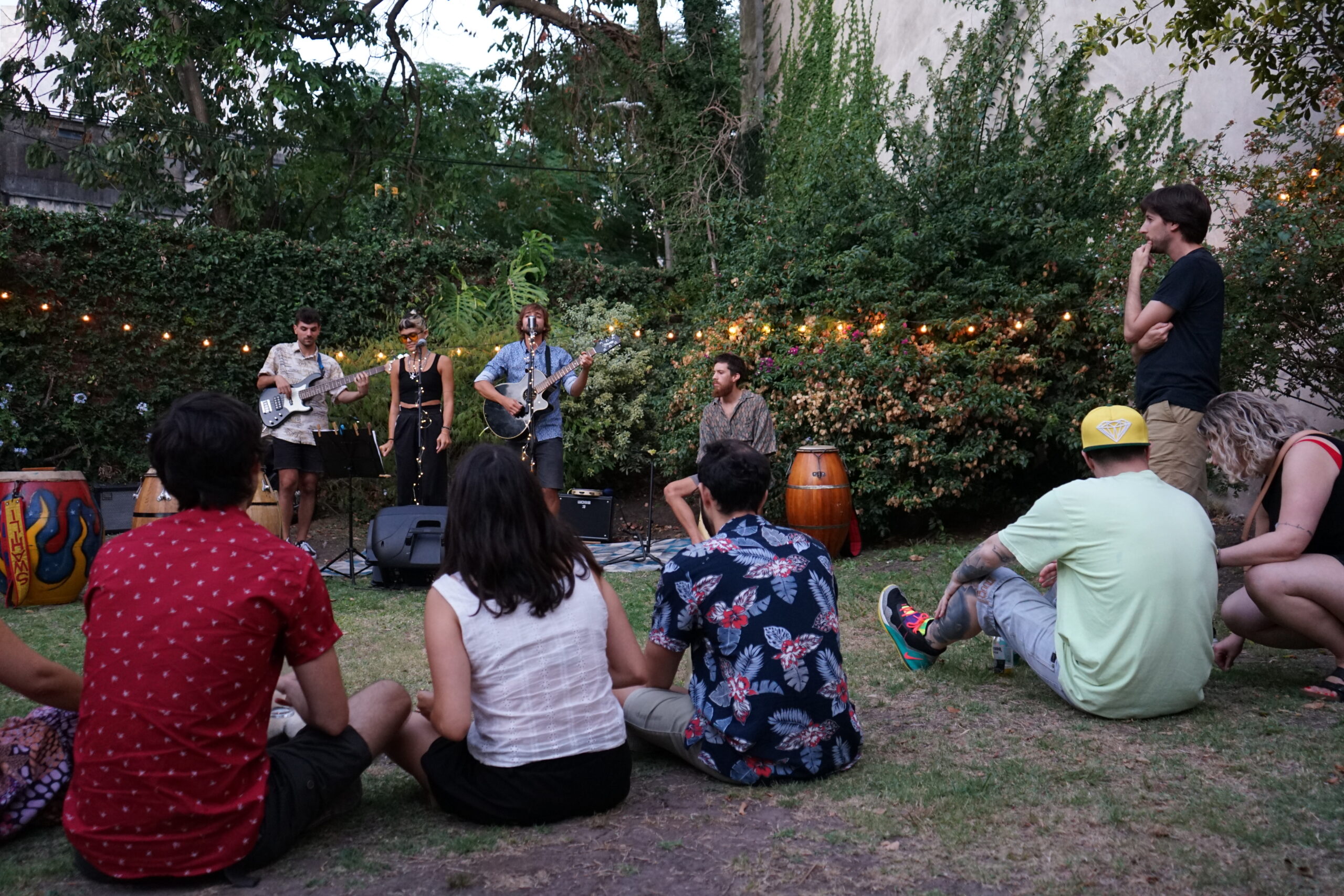 An outdoor evening gathering in a garden, with attendees sitting on the grass