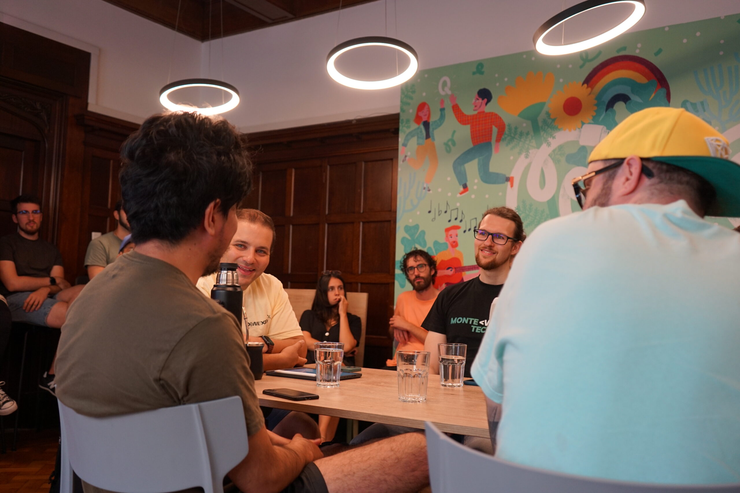 Participants talking around a table during Summer Camp 2023, with a colourful mural behind them