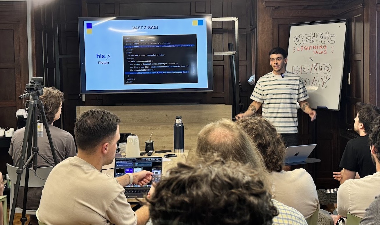 A speaker presenting to the audience beside a screen